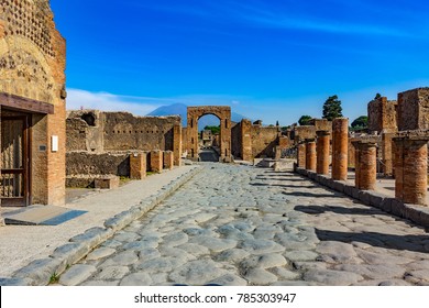 Italy. Ancient Pompeii (UNESCO World Heritage Site). Paving stones of Via del Foro. There is Arch of Caligula, Via di Mercurio and Mount Vesuvius in the background