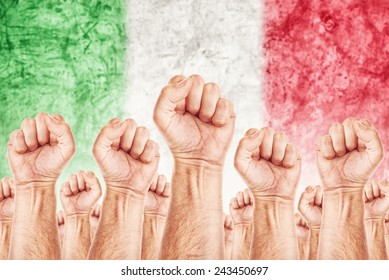 Italy Labor Movement, Workers Union Strike Concept With Male United Fists Raised In The Air Fighting For Their Rights, Italian National Flag In Out Of Focus Background.