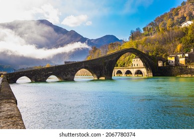 Italy, province of Lucca. Fancy Medieval Bridge - Devil's Bridge crosses the Serchio River. The green emerald cold water of the river reflects the ancient asymmetrical arches of the bridge