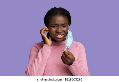 Itchy Face. Displeased Young Black Woman Scratching Skin After Wearing Protective Medical Mask, Having Allergy, Looking At Camera With Sad Expression, Isolated On Purple Background With Copy Space