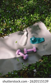 The items include a yoga mat, two dumbbells, a white water bottle. This image portrays the convenience of exercising outdoors, with the simplicity of the essentials for a workout.
