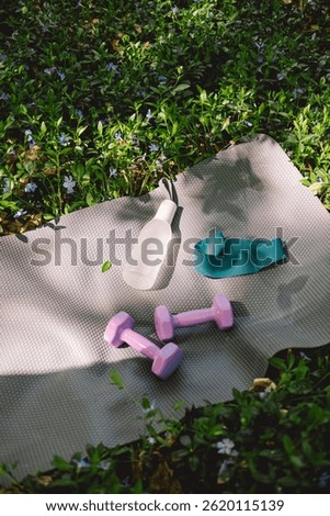 The items include a yoga mat, two dumbbells, a white water bottle. This image portrays the convenience of exercising outdoors, with the simplicity of the essentials for a workout.