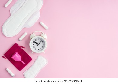 Items for intimate feminine hygiene and white alarm clock on pink background. The concept of female menstruation. Selective focus, copy space