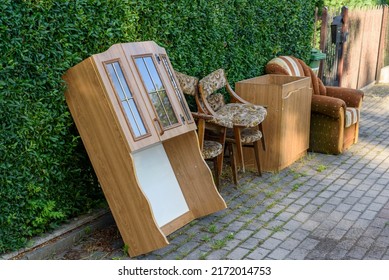 Items And Old Furniture On Street Outside House Moving Day Or Getting Rid Of Junk And Household Storage Concept. Old Damaged Furniture Extruded On A Pile Of Unnecessary Things On The Pavement.