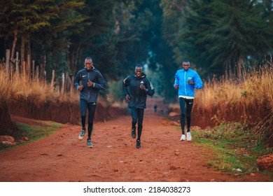 ITEN, KENYA, 22 JANUARY, 2022: Group Of Kenyan Athletes Train On Red Roads In Iten. Training Camp Of Marathon Runners Who Prepared For World AThletics Championship. Morning Scenery, War Orange Light