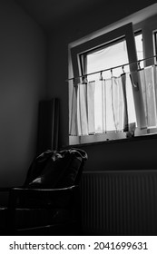 Itzehoe, Germany - Jul 2010: View Of Empty And Dark Room With Bright Sunlight Through Glass Window With Curtain. Chair And Heater Below The Window. Black And White Image. No People.