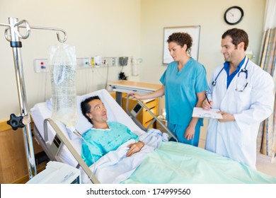 IV bag hanging on rod with medical team looking at patient in hospital room - Powered by Shutterstock