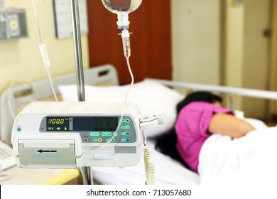 IV Drip Chamber, Tubing, And Bag Of Solution Against Blur Asian Patient Girl Resting On Hospital Bed.Inpatient During Treatment Concept.In Selective Focus.Blue Vintage Tone