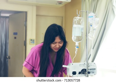 IV Drip Chamber, Tubing, And Bag Of Solution Against Blur Asian Patient Girl Resting On Hospital Bed.Inpatient During Treatment Concept.In Selective Focus.Blue Vintage Tone