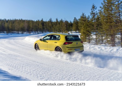 IVALO, FINLAND - February 28, 2022: Bright yellow Volkswagen Golf drives fast on a snow road during sunny day in polar Finland.