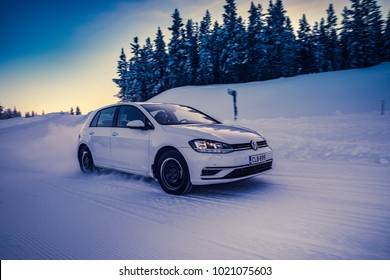 IVALO, FINLAND - February 4, 2018: White hatchback car VW Golf accelerates on a flat snow surface in Lapland during a sunny day. Naturally blurred winter forest background. Color toning applied.