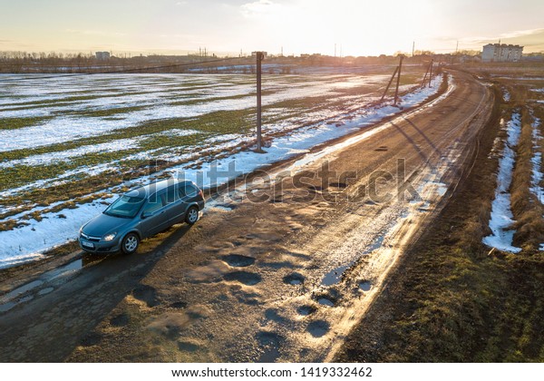 Ivano-Frankivsk, Ukraine- December 25, 2019: Aerial\
view of car moving along muddy rural road in bad condition on sunny\
spring or winter\
day.