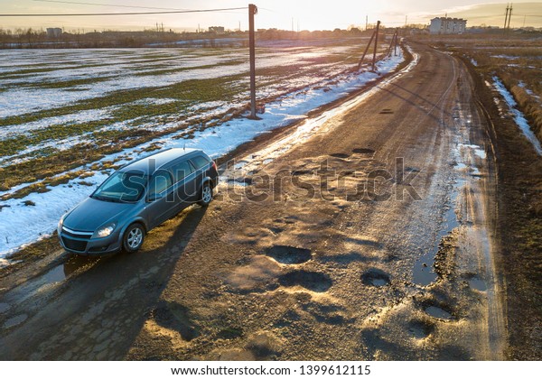 Ivano-Frankivsk, Ukraine - May 6, 2019: Aerial view\
of car moving along muddy rural road in bad condition on sunny\
spring or winter\
day.