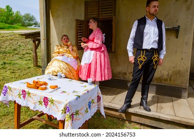 Ivanovo, Vojvodina, Serbia - April 17, 2016: Two Girls With One Guy Wearing A Traditional Folk Costume, Are Enjoy Eating Fresh Baked Donuts With Sugar At Outdoor In Shade.