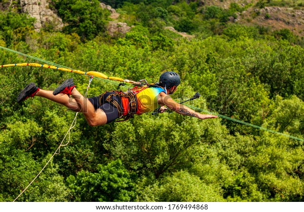 Ivanovsky Bridge, Ukraine - June 21, 2020: Concept\
of Extreme Sports and Fun. A man is  doing rope jumping from the\
bridge. He is very happy to make a dream come true.  He is sporty\
and in a good form