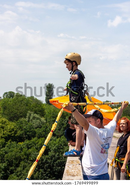 Ivanovsky\
Bridge, Ukraine - June 21, 2020: Concept of Extreme Sports and Fun.\
An instructor helps a small boy to jump with a rope  from the\
bridge. All equipment is very firmly\
fixed