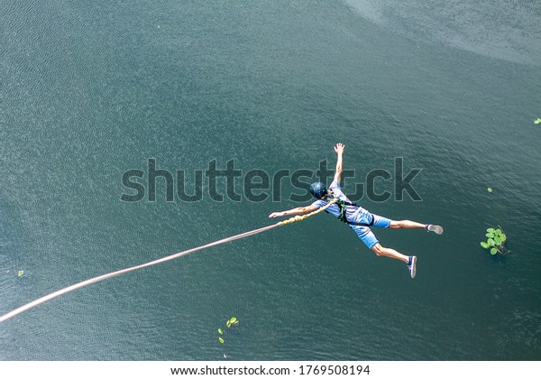 Ivanovsky Bridge, Ukraine - June 21, 2020: Concept\
of Extreme Sports and Fun. A man is  doing rope jumping from the\
bridge. He is happy to make a dream come true. \
All equipment is\
very firmly fixed