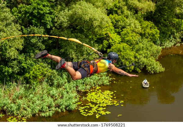 Ivanovsky Bridge, Ukraine - June 21, 2020: Concept\
of Extreme Sports and Fun. A man is  doing rope jumping from the\
bridge. He is very happy to make a dream come true.  He is sporty\
and in a good form
