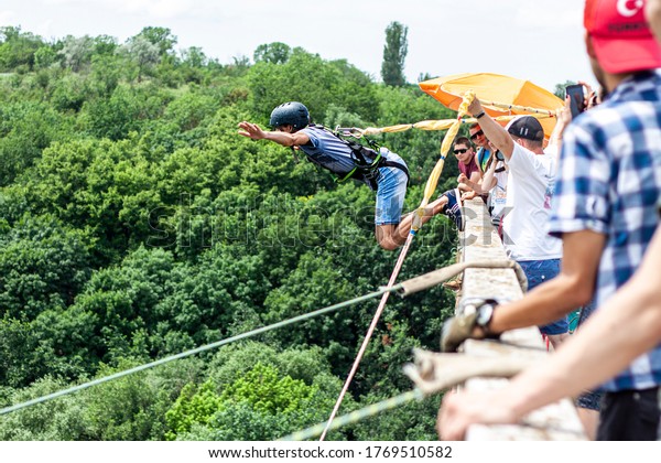 Ivanovsky Bridge, Ukraine - June 21, 2020: Concept\
of Extreme Sports and Fun. A man is  doing rope jumping from the\
bridge. He is happy to make a dream come true. \
All equipment is\
very firmly fixed