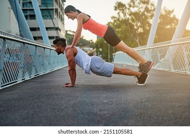 Ive got your back. Shot of a young woman balancing on her boyfriends back while doing pushups outdoors on a bridge.