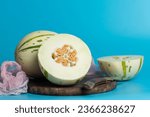 Ivory gaya melon with green dotted stripes and spots on a blue background. Colorful ripe juicy and soft fruit, sweet taste with floral notes. Whole and half melons on a wooden cutting board