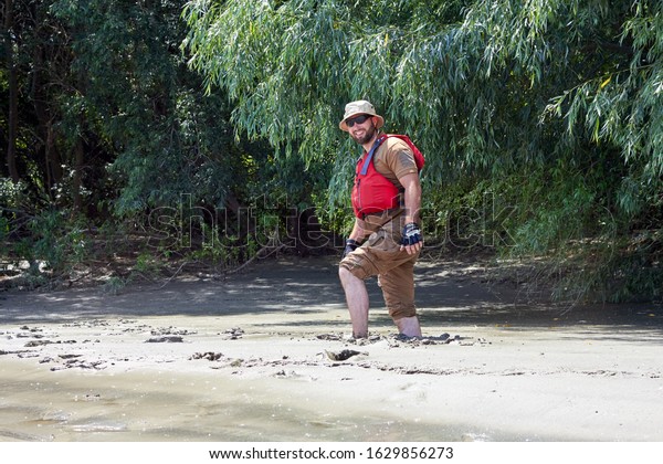 IZMAIL, UKRAINE - July 13, 2019: Man standing in\
natural quicksand river, clay sediments, sinking, drowning quick\
sand, stuck in the soil