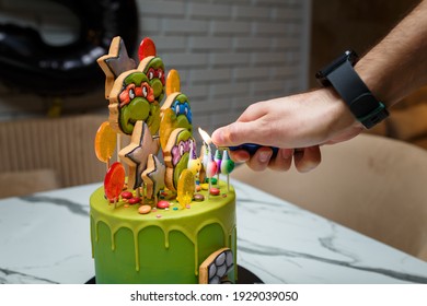 Izmail, Ukraine. November 2020. Hand with lighter kindling candles on birthday cake with teenage mutant ninja turtles cartoon characters. Boy happy birthday festive party.