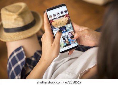 IZMIR ,TURKEY - JUNE 27, 2017: Smartphone Samsung Galaxy S8 Plus Orchid Grey Color. Young Women with black nail polish Open apps INSTAGRAM application on the screen on rustic brown wood background.