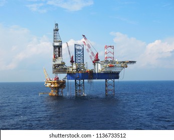 Jack up drilling rig operates over offshore wellhead platform with blue sea background. - Shutterstock ID 1136733512