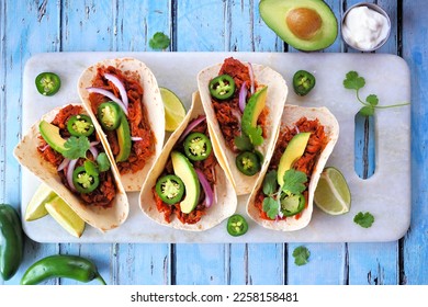 Jack fruit vegan tacos. Top down view table scene over a rustic blue wood background. Healthy eating, plant-based pulled pork meat substitute.