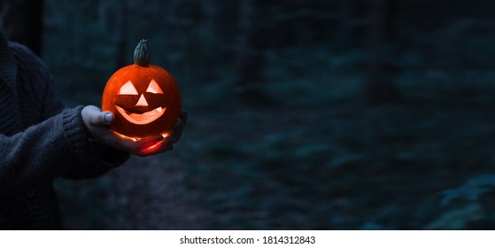 Jack O Lantern Glowing With Moonlight On In Eerie Night Forest. Halloween Bokeh Background With Burning Orange Pumpkin That A Men Holds In His Hands. Happy Halloween Banner. Copy Space For Text