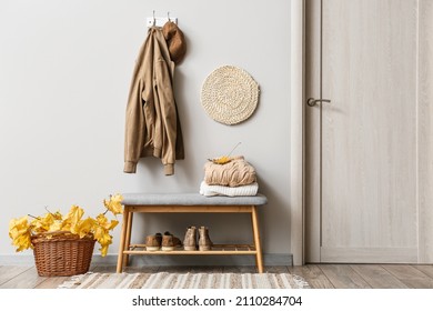 Jacket and hat hanging on light wall and basket with autumn leaves in interior of stylish hallway