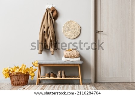 Jacket and hat hanging on light wall and basket with autumn leaves in interior of stylish hallway