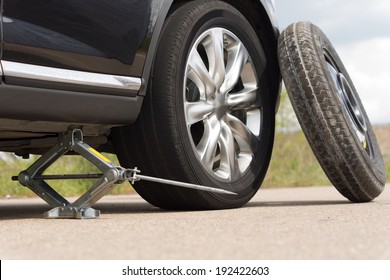 Jacking up a car to change a tyre after a roadside puncture with the hydraulic jack inserted under the bodywork raising the vehicle and the spare wheel balanced on the side
