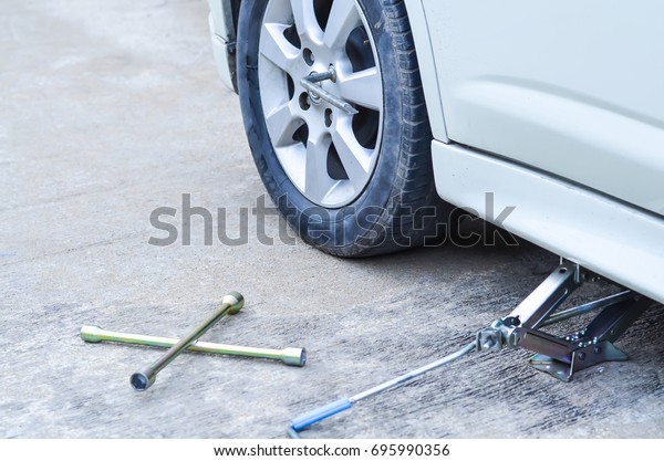 Jacking up a car to\
change a tyre after a roadside puncture with the hydraulic jack\
inserted under the bodywork raising the vehicle and the spare wheel\
balanced on the side