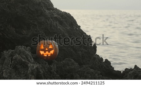 Jack-O'-Lantern Pumpkin with Flickering Candlelight Inside Stands on Sharp Rocks in the Sea. Halloween Scene.