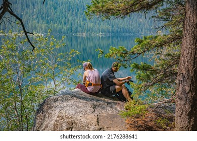 Jackson Hole, Wyoming, USA - Sept 15, 2020: A Couple Hiking In The Mountains Around A Lake That Have Taken A Rest On A Large Rock Beside The Lake.