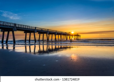 Jacksonville Beach, Florida / USA - July 11, 2017: The beautiful blue and golden sky on an cool summer sunrise at the pier; a fisherman in the distance enjoying the morning