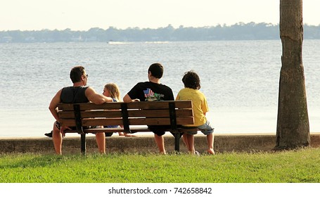 JACKSONVILLE, FLORIDA - JULY 15, 2013: Father And Three Children Sitting On The Bench Near The Lake In Jacksonville, Florida