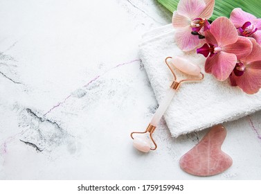Jade face roller for beauty facial massage therapy with towel and orchid flowers. Flat lay on marble background