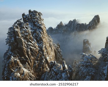 Jagged, snow-capped peaks rise sharply through a misty atmosphere, with sunlight casting dramatic shadows on rugged rock faces. - Powered by Shutterstock