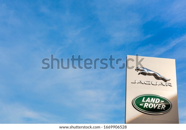 Jaguar Land Rover brand logo on bright blue sky\
background located on its dealer office building in Lyon, France -\
February 23, 2020