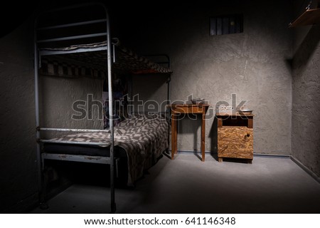 Jail cell with iron bunk bed and wooden bedside table with aluminum dishes