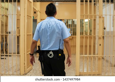 Тюремщик проходит через тюремный проход, входит в безопасную зону. Сотрудник тюрьмы в синей рубашке с наручниками и дубинкой обходит коридор тюрьмы.