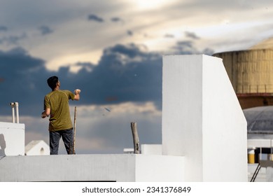 Jaipur, Rajasthan - 14th Jan 2023: Slow motion shot of man on roof of white building flying kite with multiple kites visible in background during the festival of sankranti, uttarayan and independence  - Powered by Shutterstock