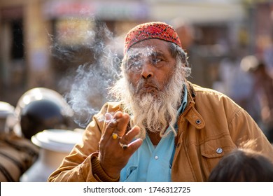 Jaisalmer, India - December 7, 2019: Portrait of an elderly Rajasthani man blowing cigarette smoke.