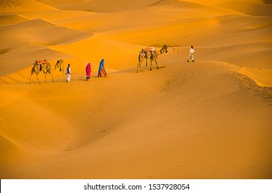 Jaisalmer, rajasthan, india - april 18th, 2018: Migrant worker people walk to their home due to covid-19, aerial view of people with camels walking on golden sand dunes Jaisalmer, Rajasthan, India