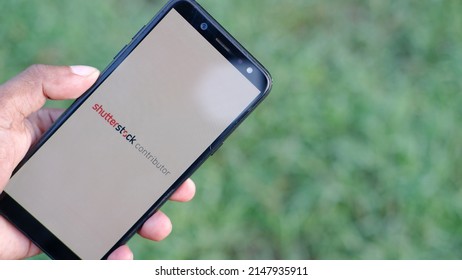 Jakarta, Indonesia - April 20, 2022: Hand holding a smartphone and open Shutterstock contributor application. Shutterstock is biggest Microstock agency for photographers selling their photos and video