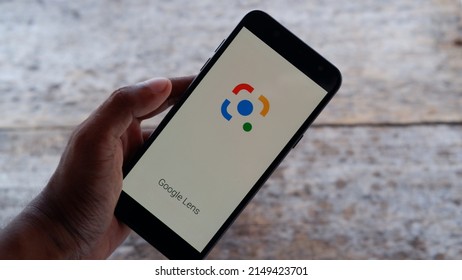 Jakarta, Indonesia - April 25, 2022: Hand holding a smartphone with Google lens application on wooden background 