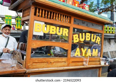 Jakarta, Indonesia -August, 2022 : Chicken Porridge Seller Carrying A Brown Wooden Cart On Sunday Morning During The Car Free Day Event. Bubur Ayam Seller Vendor.